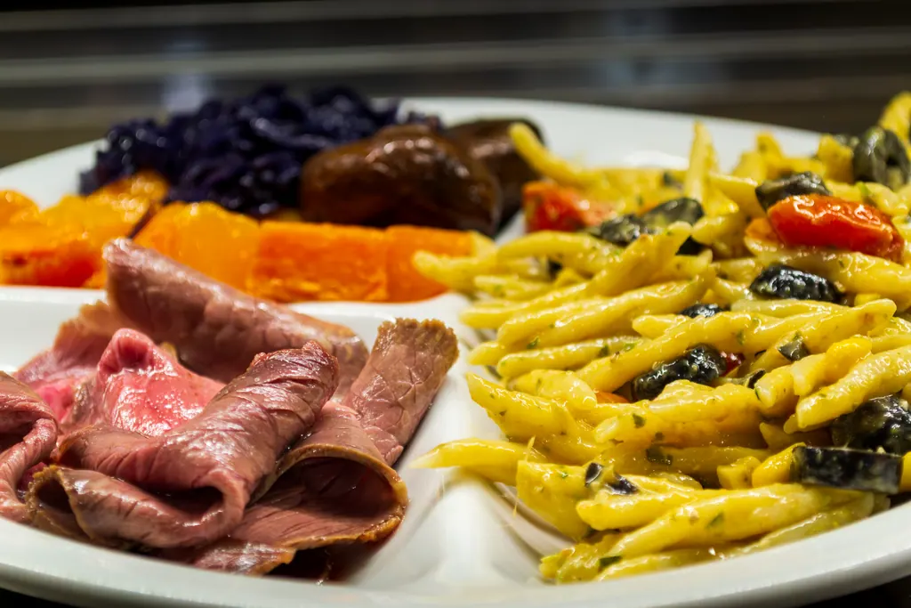 Piatto della tavola calda con pasta, verdure e affettati
